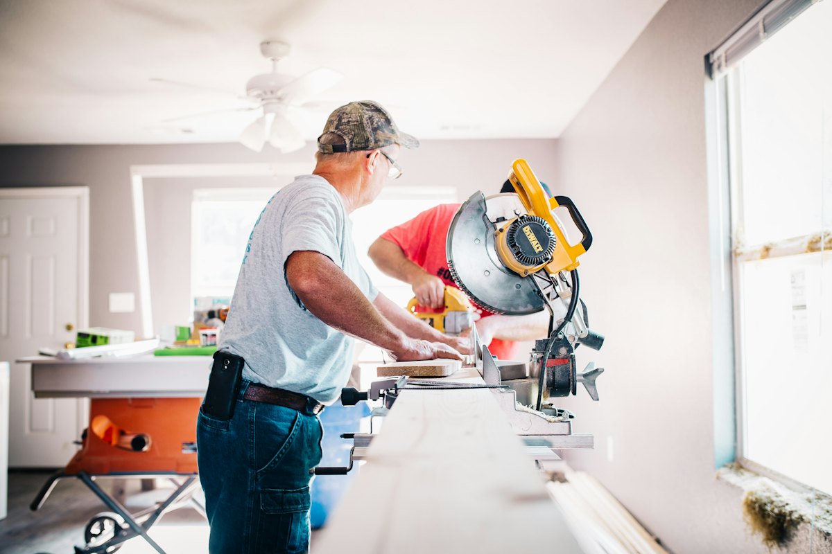 Two workers cutting trim with a mitre saw in a room being renovated